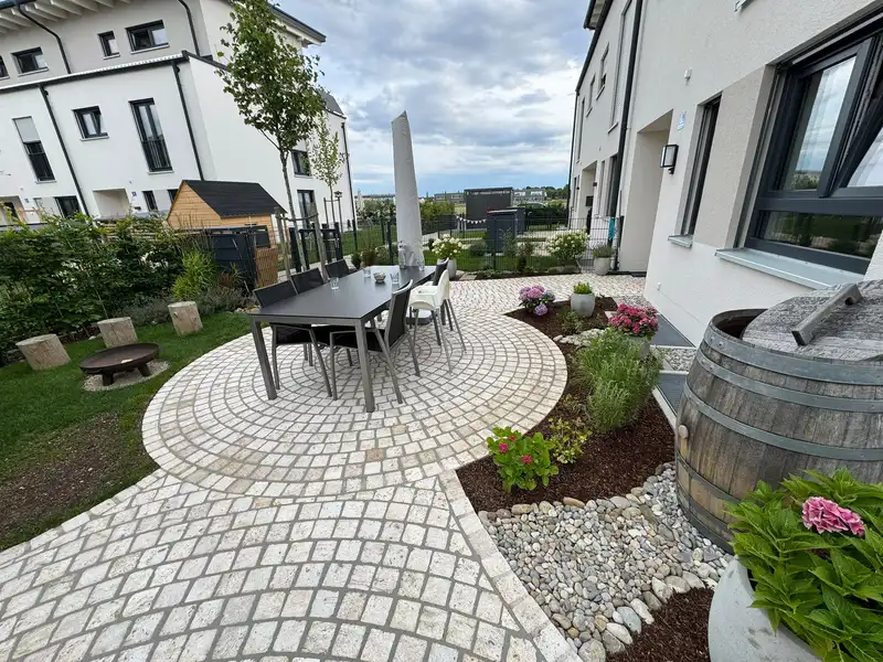 Derselbe Platz fertig: runder Kleinpflaster-Sitzplatz mit Esstisch und Beeten
