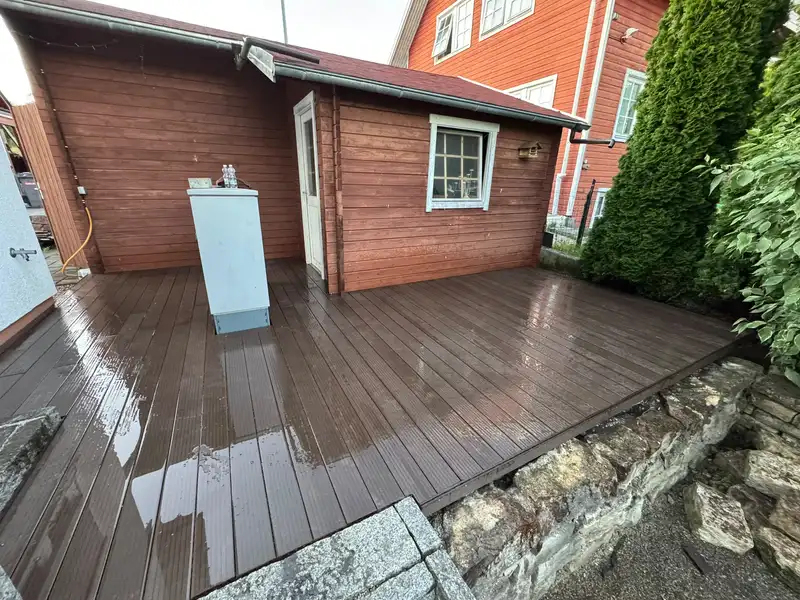 Dunkelbraune Holzterrasse vor einem Gartenhaus