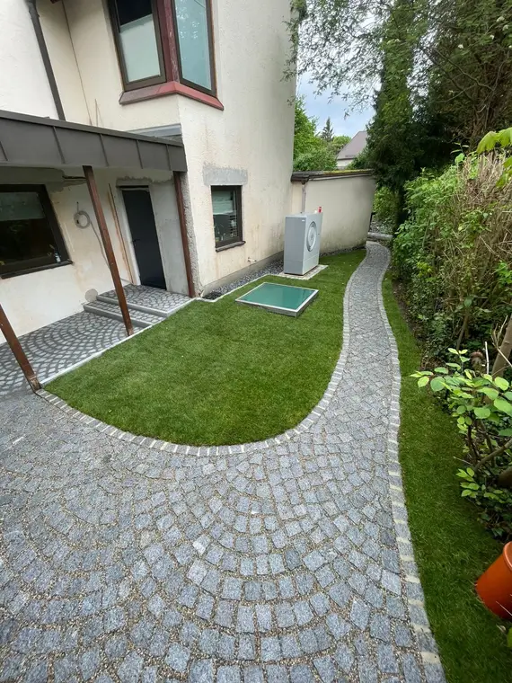 Gepflasterter Gartenweg und Rasenfläche neben einem Wohnhaus