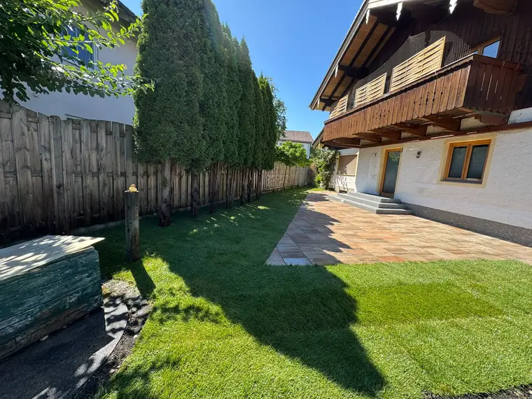 Pflasterter Gartenbereich mit Rasen, Zaun und Wohnhaus