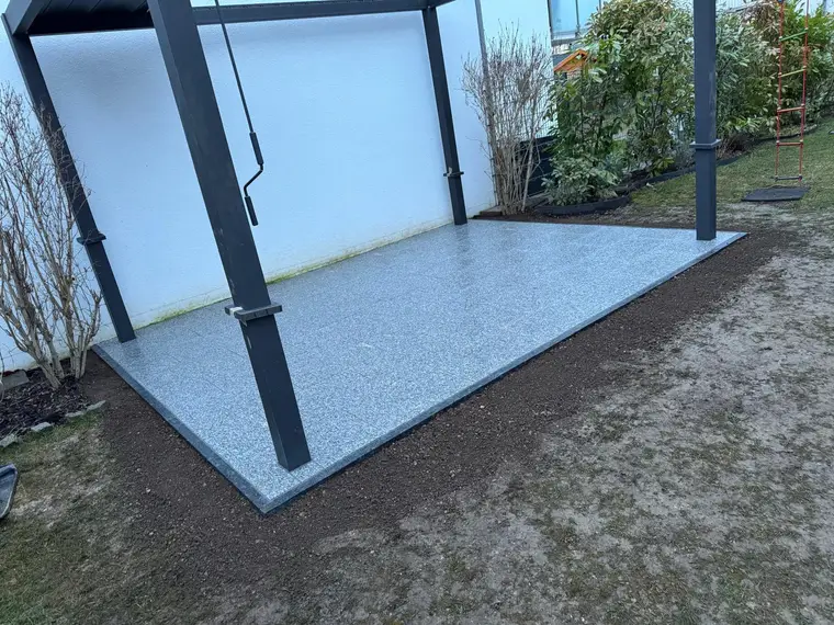 Neue Terrassenüberdachung mit grauem Fliesenboden im Garten