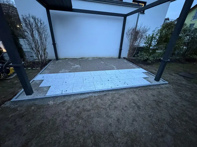 Teilweise verlegte Terrassenplatten unter einer dunklen Überdachung