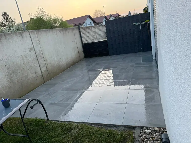 Nasse Geflieste Terrasse mit Betonmauer und Sichtschutzzaun