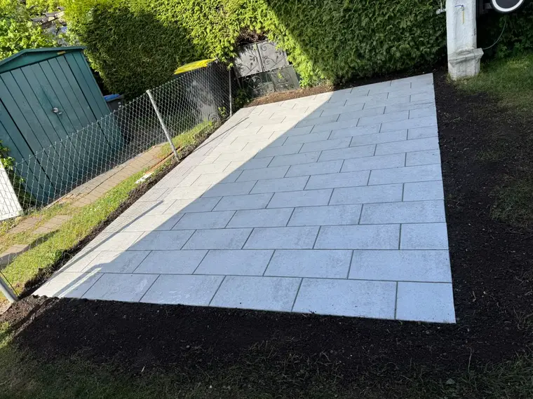 Frisch gepflasterte Terrassenfläche im Garten neben Hecke und Schuppen