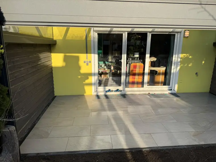 Geflieste Terrasse vor einer gelben Hauswand mit Glas-Schiebetür