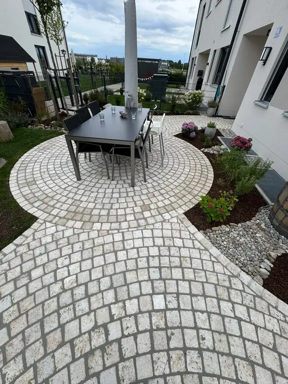 Gepflasterte Terrasse mit Esstisch und Stühlen vor Reihenhäusern