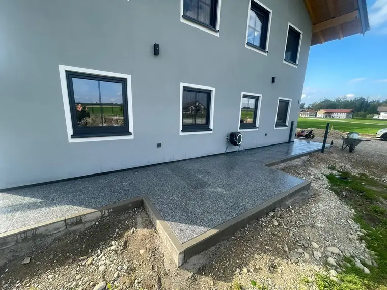 Außenansicht eines grauen Hauses mit neu gepflasterter Terrasse