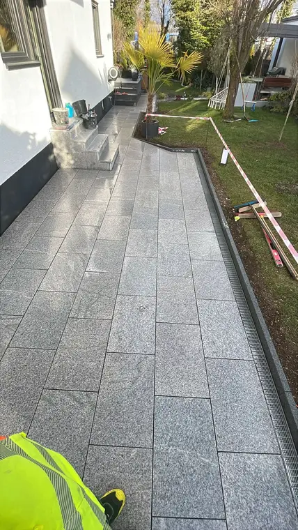 Neu gefliester Terrassenbereich mit grauen Granitplatten neben dem Garten