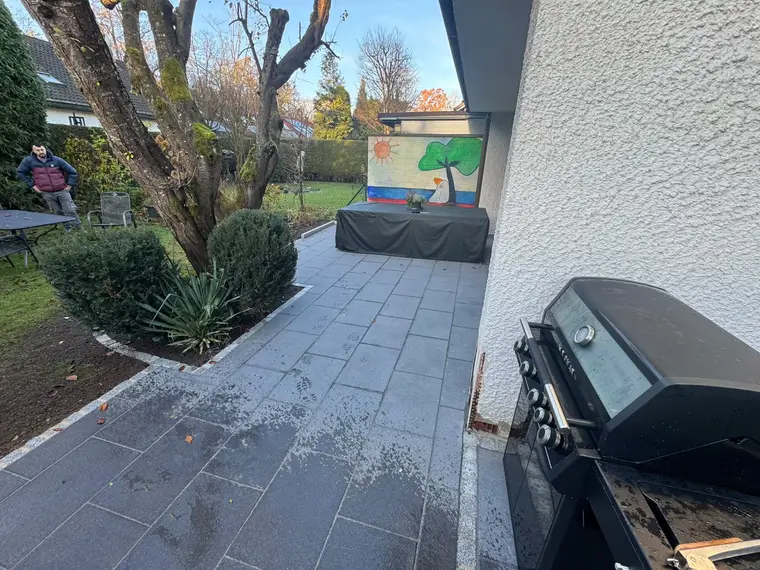 Pflasterter Gartenbereich mit Grill, Bäumen und bunter Wandmalerei