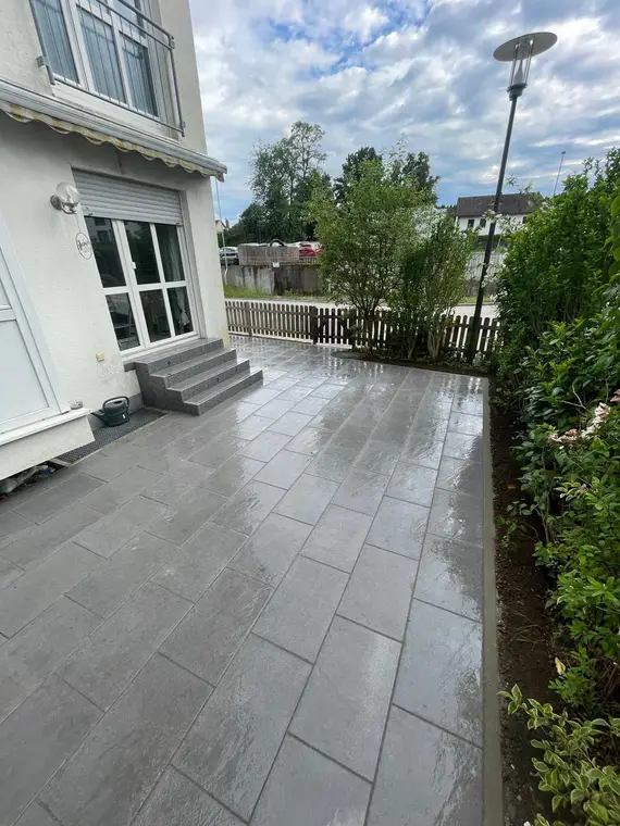 Gepflasterte Terrasse an einem Wohnhaus mit Garten