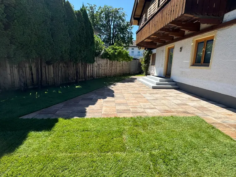 Gepflasterte Terrasse mit Rasen und Holzzaun am Haus