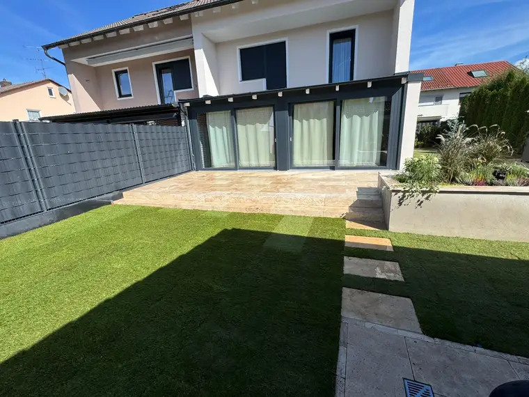 Moderne Terrasse mit Rasenfläche und Wintergarten an Wohnhaus