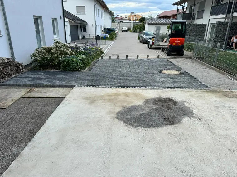 Gepflasterter Einfahrtsbereich mit Kieshaufen und rotem Minibagger