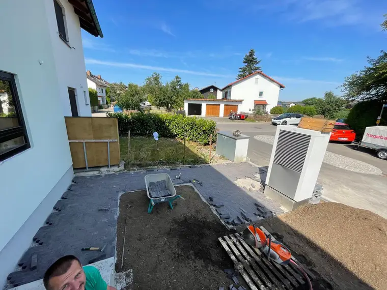 Pflasterarbeiten im Garten mit Schubkarre und Wärmepumpe