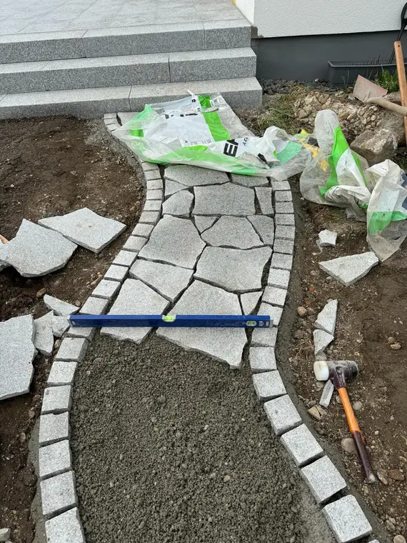 Angelegter Gartenweg aus Natursteinplatten mit Wasserwaage und Werkzeug