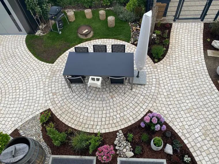 Gepflasterter Gartenbereich mit Esstisch, Rasen und Blumenbeeten aus der Vogelperspektive