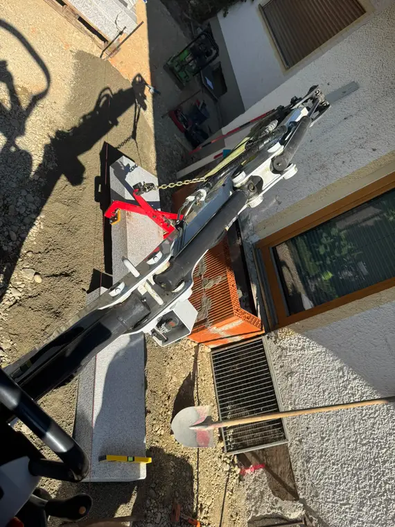 Baggerarm setzt Granitstufen an einer Hauswand ein