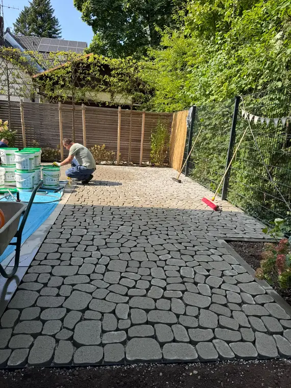 Handwerker verfugt eine Pflasterfläche im Garten