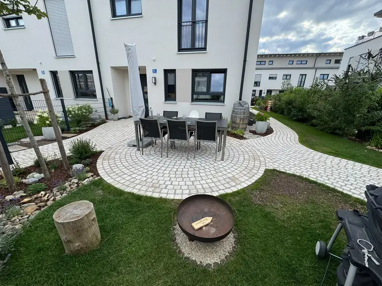 Pflasterter Gartenbereich mit Sitzgruppe, Feuerschale und Rasen