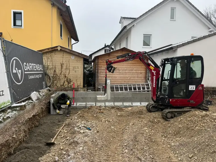 Minibagger setzt L-Steine auf einer Baustelle im Garten
