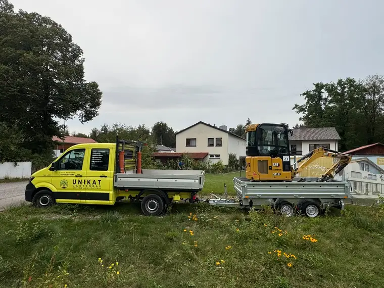 Gelber Pritschenwagen von Unikat Gartenbau mit Minibagger auf Anhänger