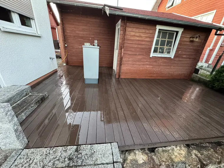 Nasse Holzterrasse vor einer Gartenhütte mit graurem Schrank
