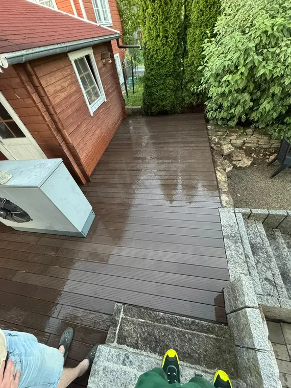 Nasse Holzplanken-Terrasse neben einem Gartenhaus mit Wärmepumpe