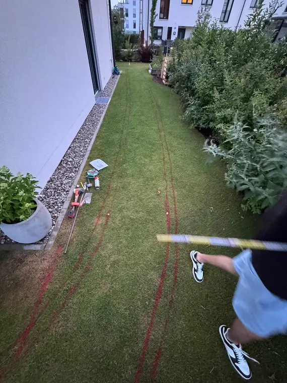 Rasenstreifen an der Hauswand mit rot markiertem Wegverlauf